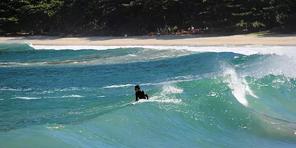 Surfista pegando onda nas águas azuis de Paraty com a praia deserta ao fundo